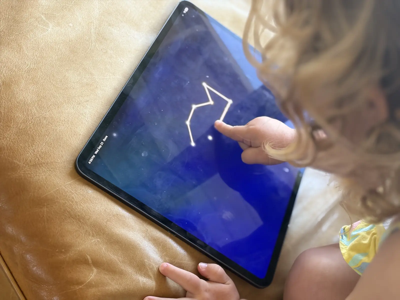 A child joins stars into a constellation with one finger on a tablet, on a sofa at home